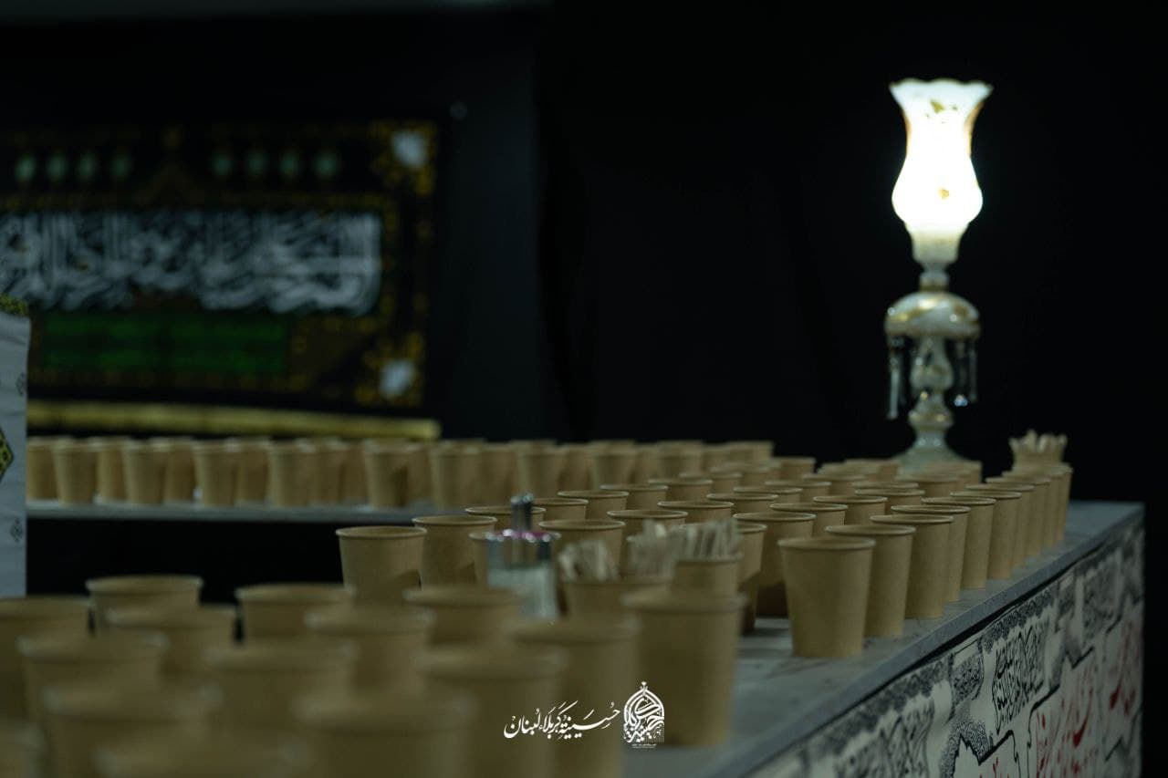Rows of paper cups prepared for mourners beside a glowing lamp and calligraphy banner